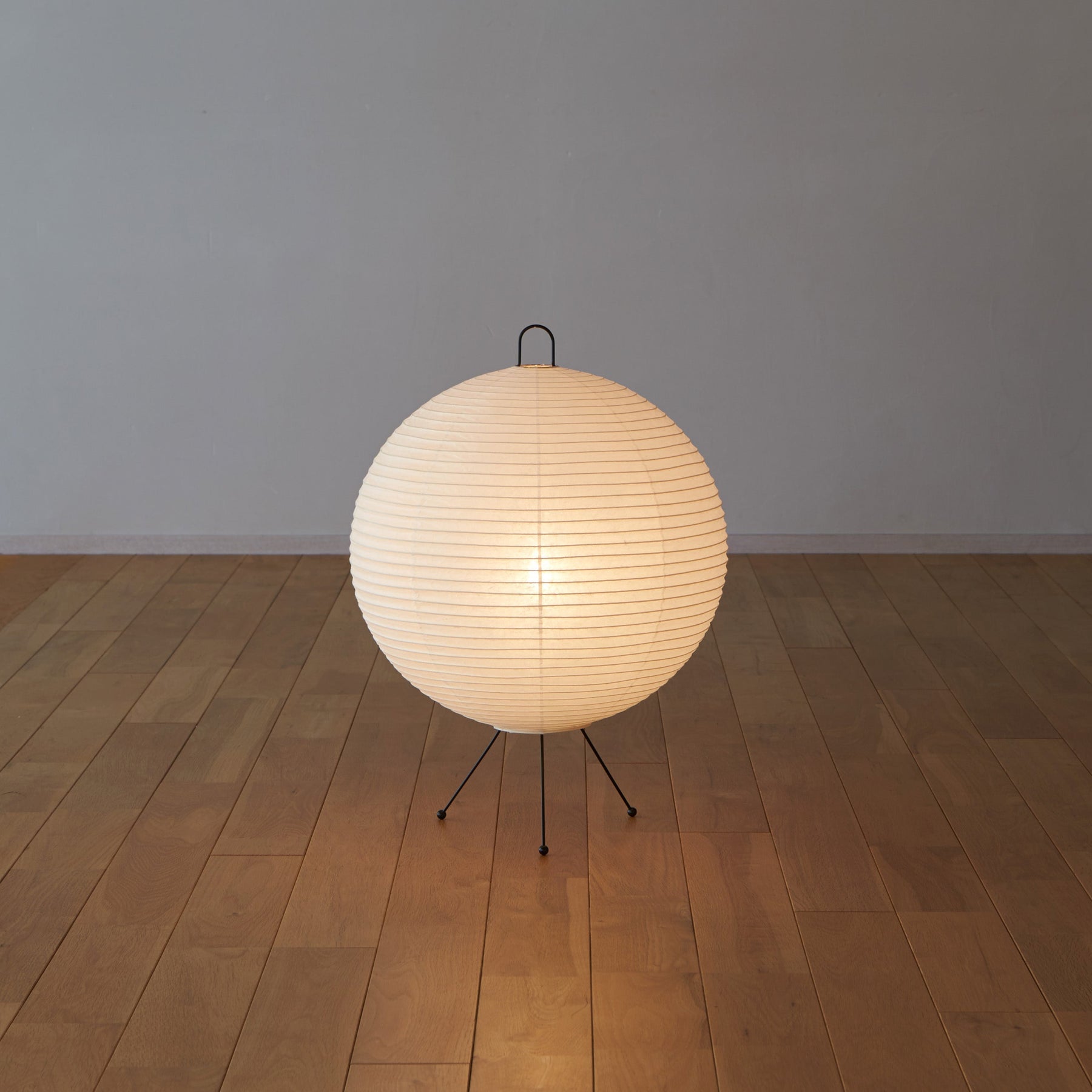 Spherical paper lamp on a wooden floor with a plain wall background