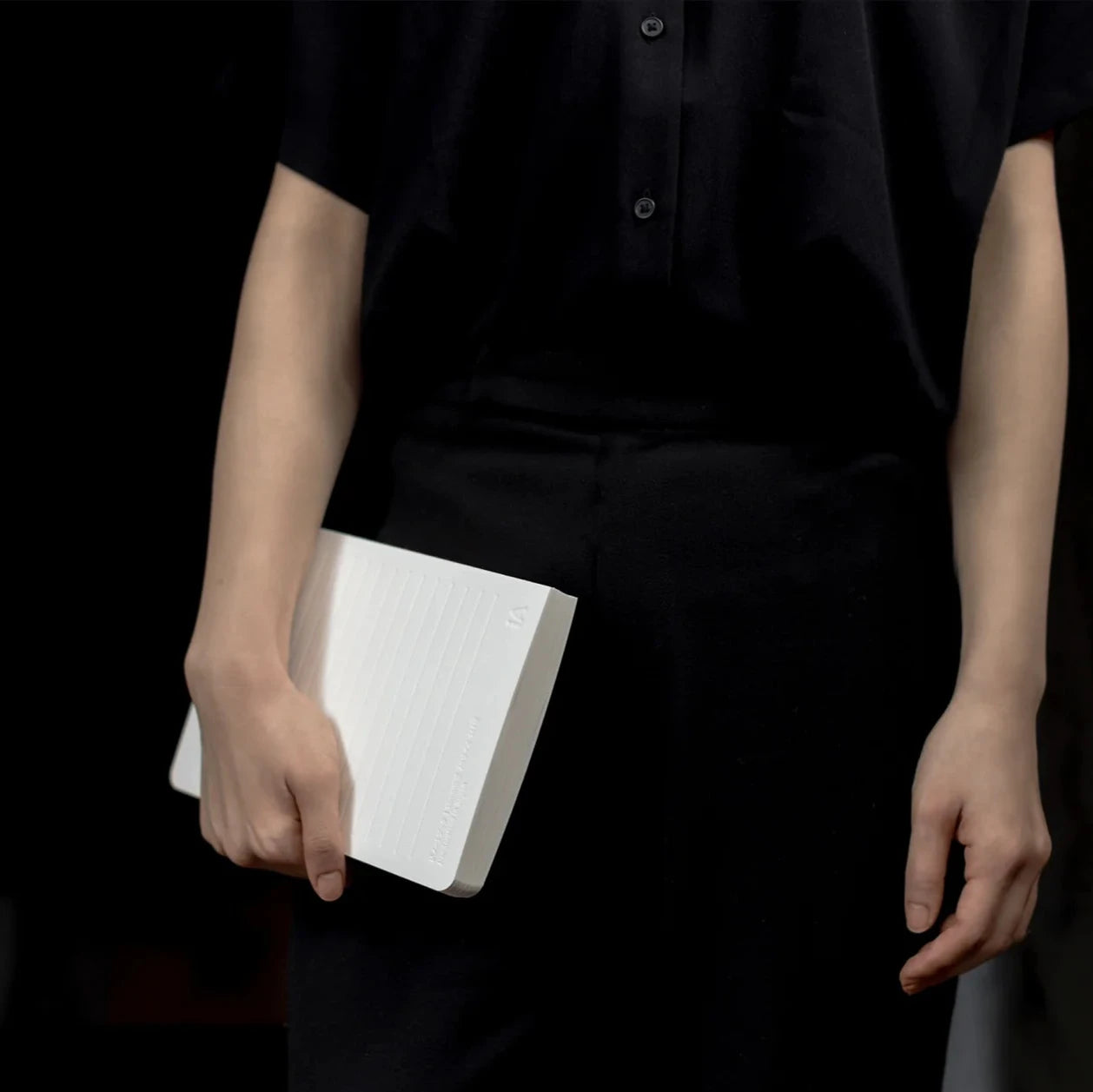 Person holding a white book against a dark background