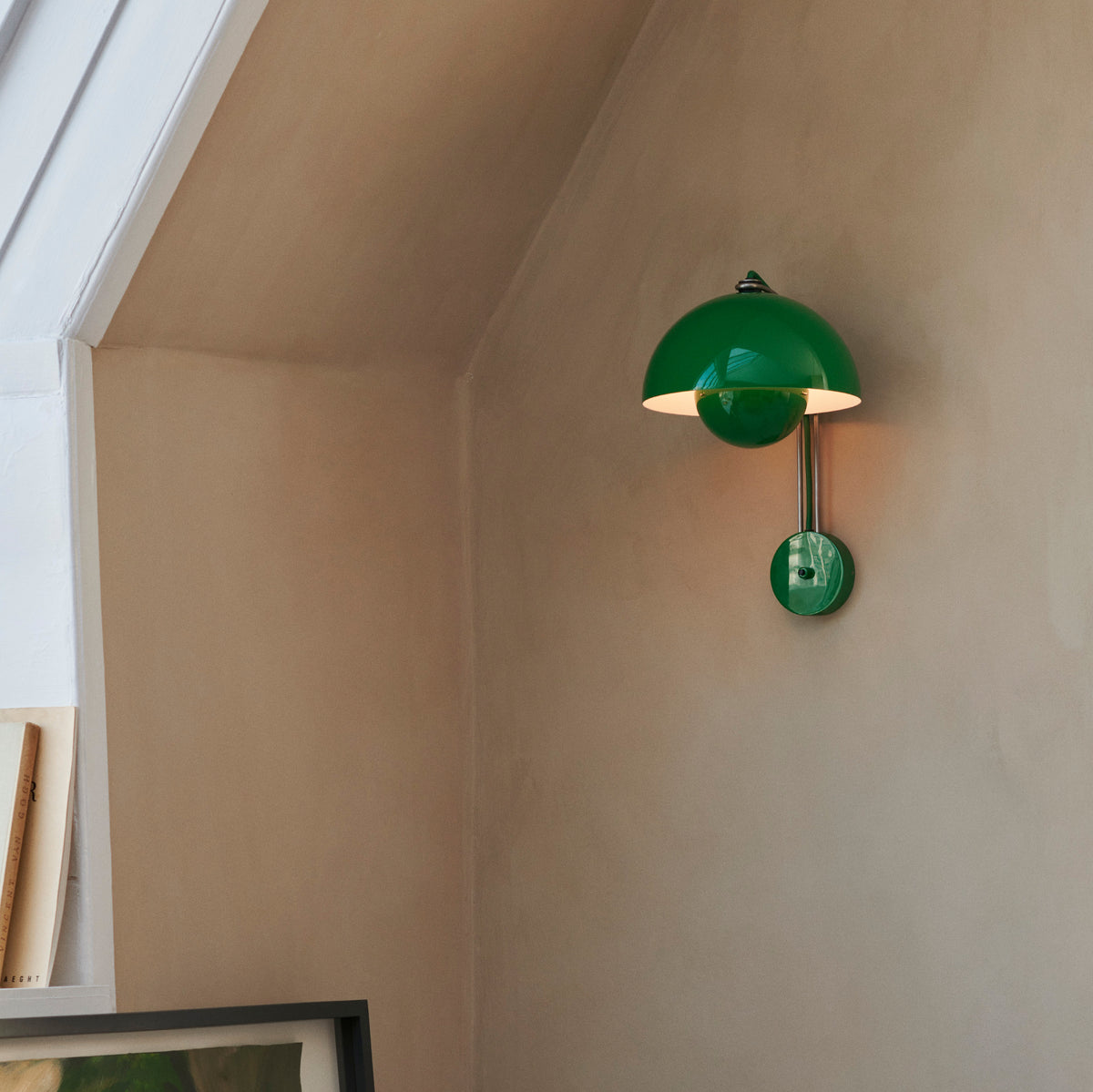 Green wall-mounted lamp on a beige wall with a window in the background