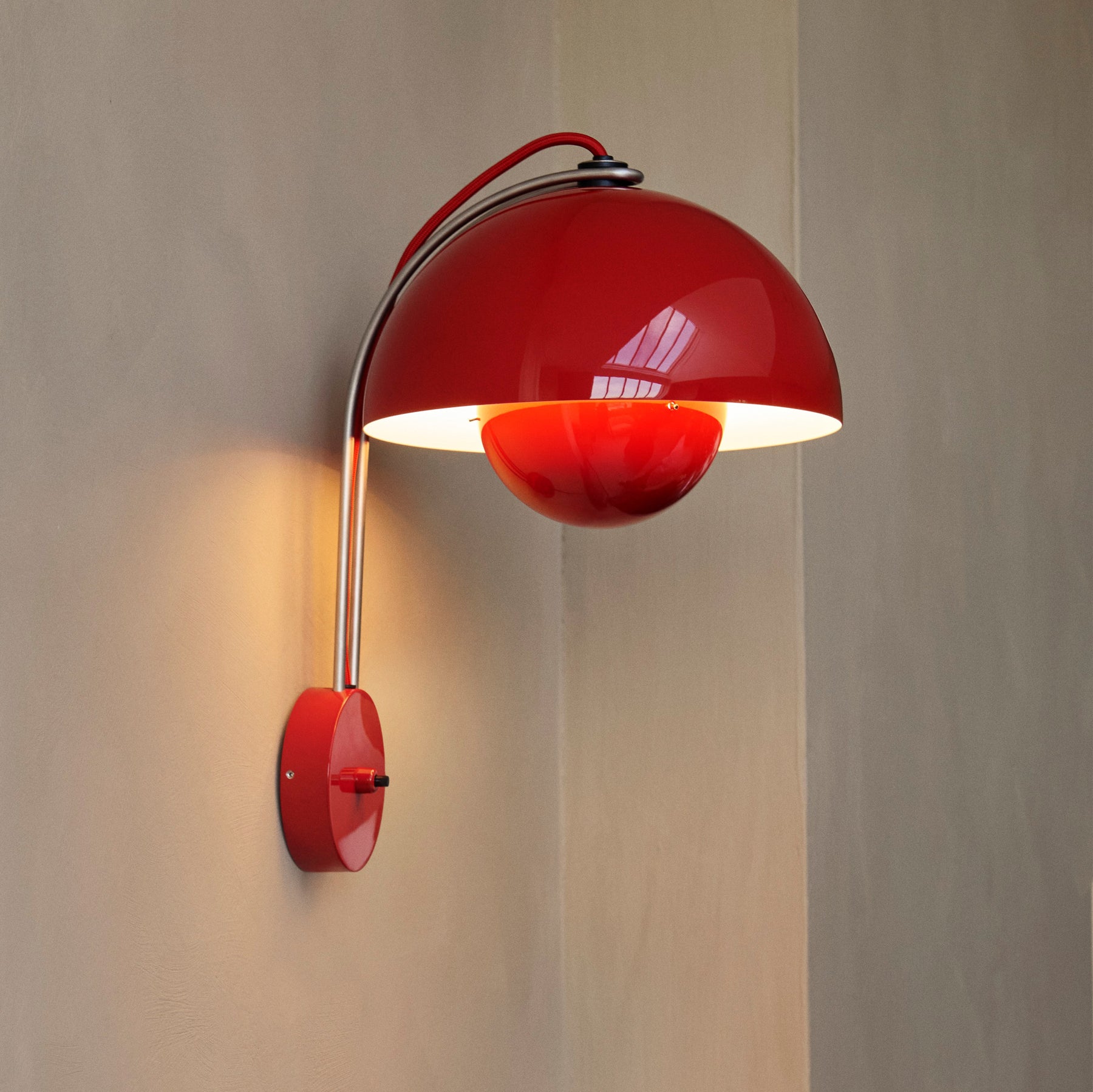 Red wall lamp with a metallic arm on a neutral background