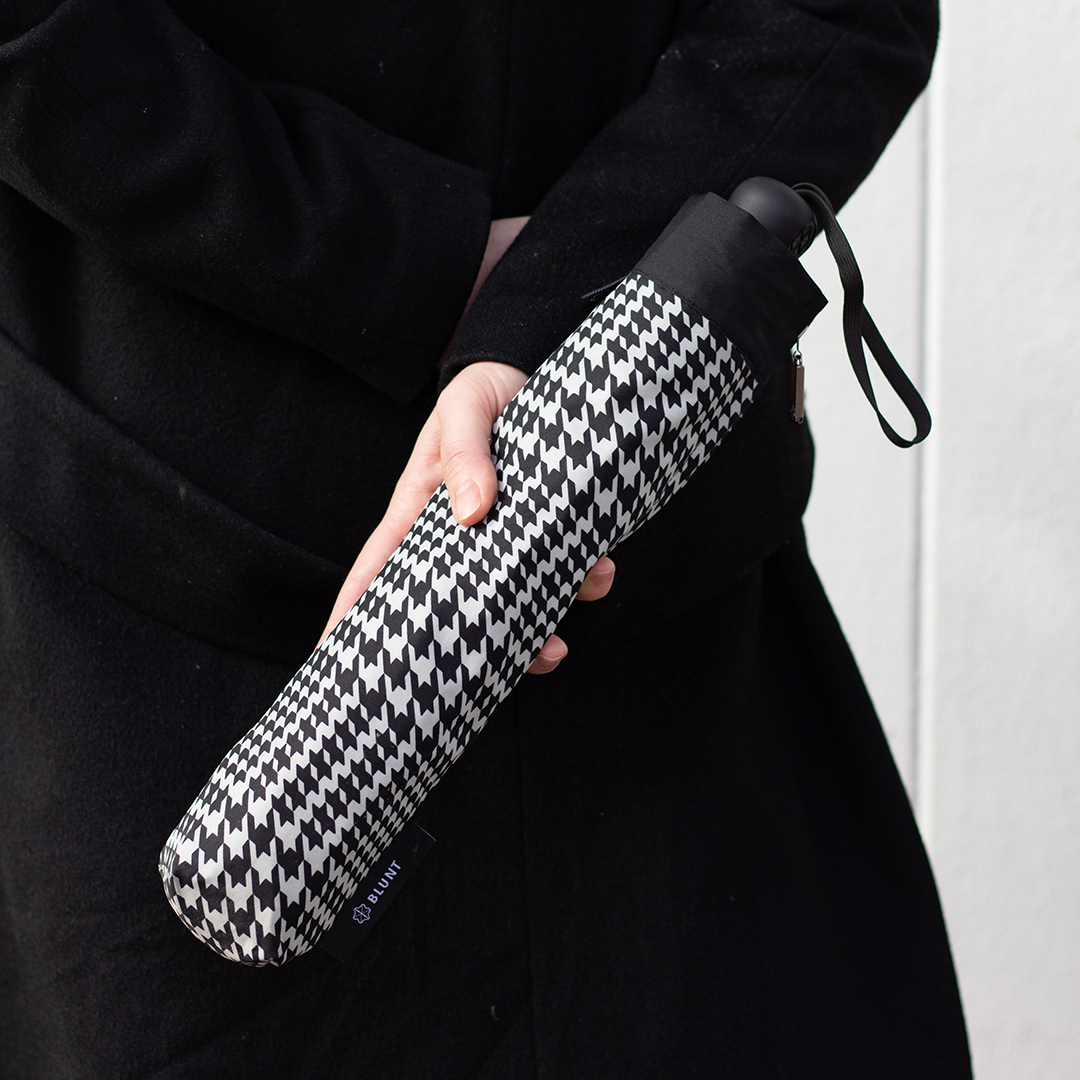 Person holding a black and white patterned umbrella against a plain background