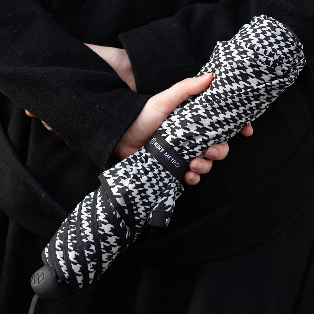 Person holding a black and white patterned umbrella with 'Saint Bester' branding.