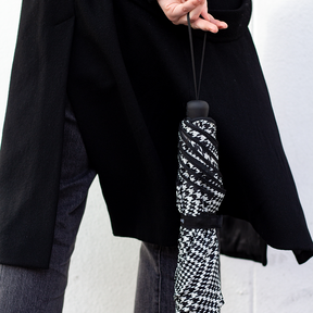 Person holding a black and white houndstooth patterned umbrella with a plain background