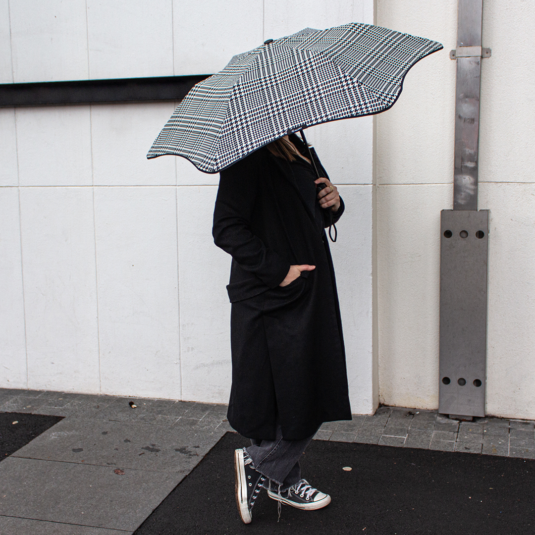 Person holding a black and white checkered umbrella against a light-colored wall.
