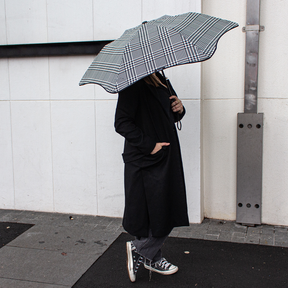 Person holding a black and white checkered umbrella against a light-colored wall.