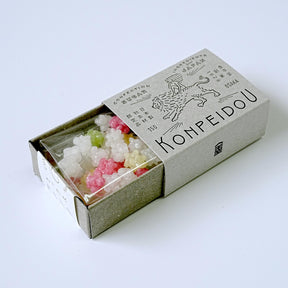 A matchbox-style package containing small translucent decorative beads or candy-like pieces in white, pink, and pale green, photographed on a clean white background. The box is printed with the brand name Kohpeidou and illustrated graphics.