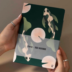 Hand holding a notebook with turtle illustrations on a plain background