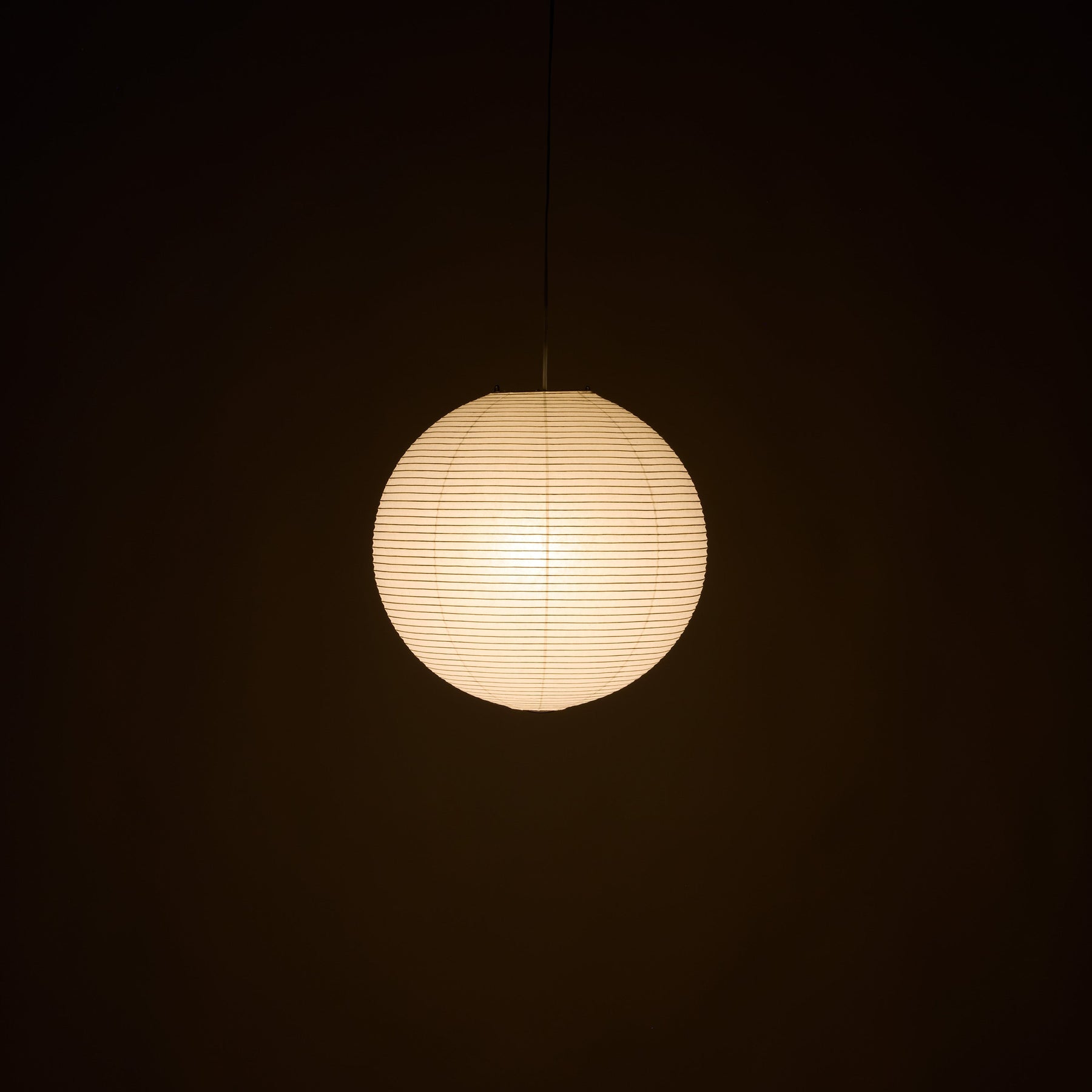 A spherical paper lantern pendant light glowing with warm cream light against a dark background.