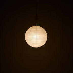 A spherical paper lantern pendant light glowing with warm cream light against a dark background.