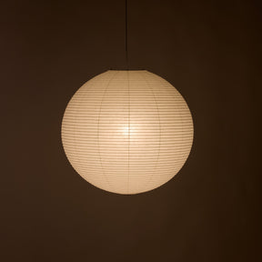 A spherical paper lantern pendant light glowing with warm cream light against a dark brown background.