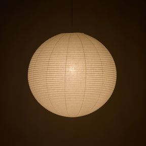 A spherical paper lantern pendant light glowing with warm cream light against a dark brown background.
