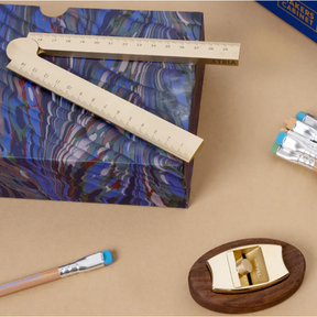 Blue marbled notebook with a ruler on top, brush, and small wooden item on a beige surface