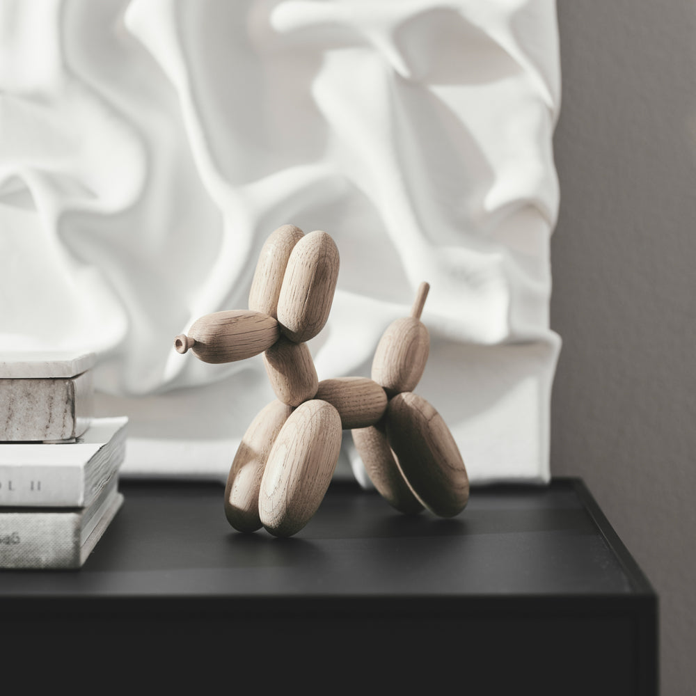 Wooden balloon dog sculpture on a black surface with a textured white wall in the background