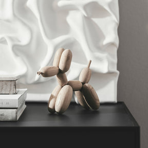 Wooden balloon dog sculpture on a black surface with a textured white wall in the background