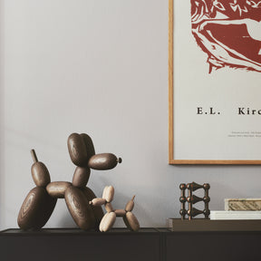 Wooden dog sculpture on a shelf with a framed poster in the background