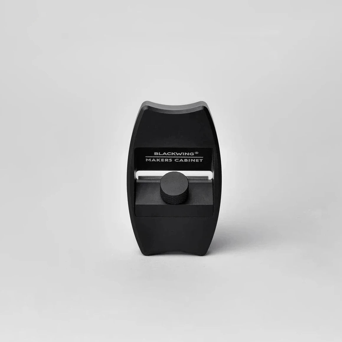 Front view of a matte black Blackwing × Makers Cabinet Høvel pencil sharpener with an adjustable knurled knob, centered on a light gray background.