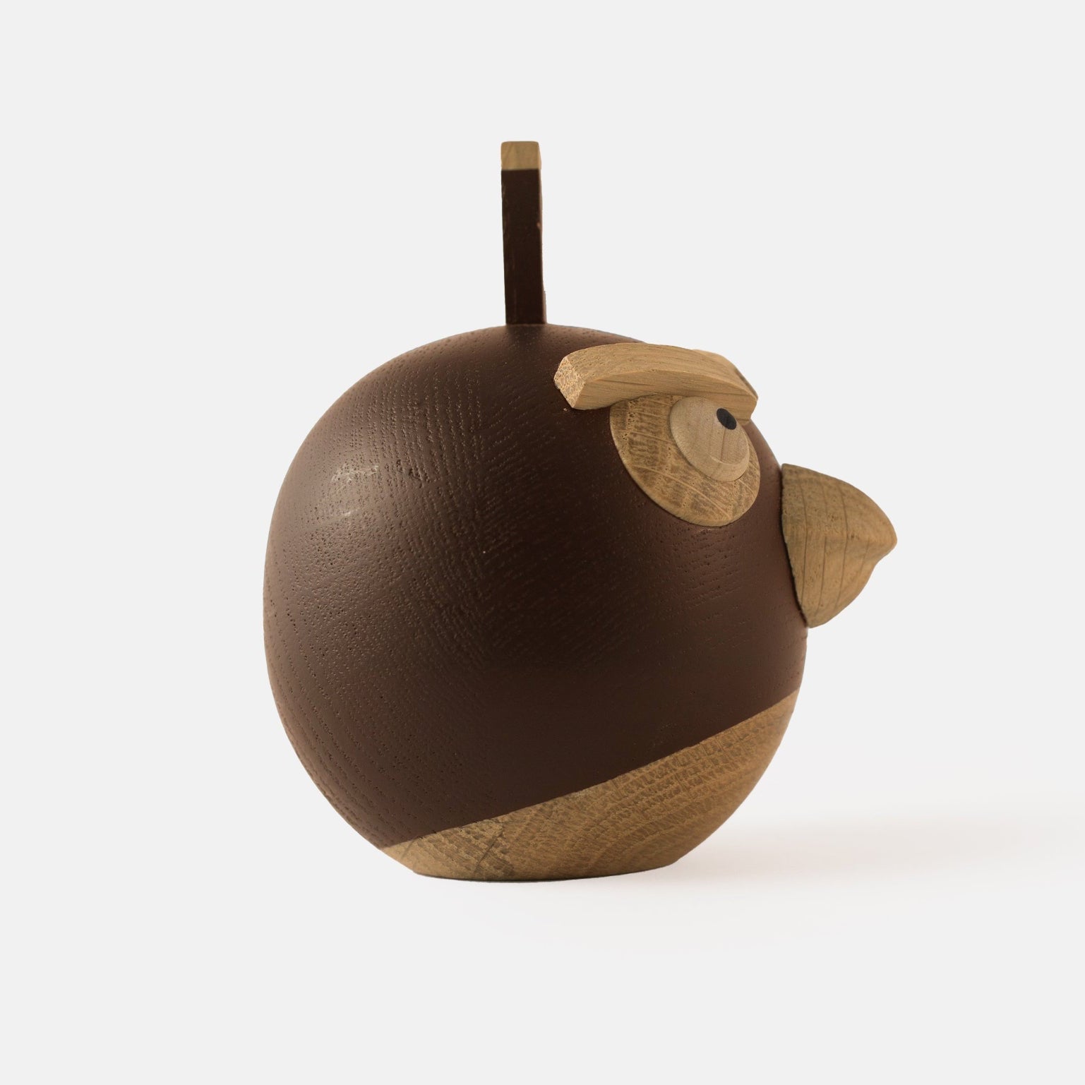 Side view of wooden figurine of an animated cartoon bird character carved from dark and light wood, featuring a round body, prominent beak, expressive eye details, a small top stem, visible natural wood grain, and a smooth matte surface on a plain white background.