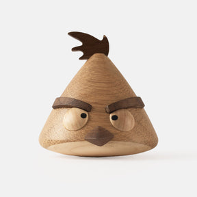 Wooden figurine of an animated cartoon bird character carved from light and dark wood, featuring a triangular body shape, prominent angled eyebrows, round eye details, a small pointed beak, visible natural wood grain, and a smooth matte surface on a plain white background.