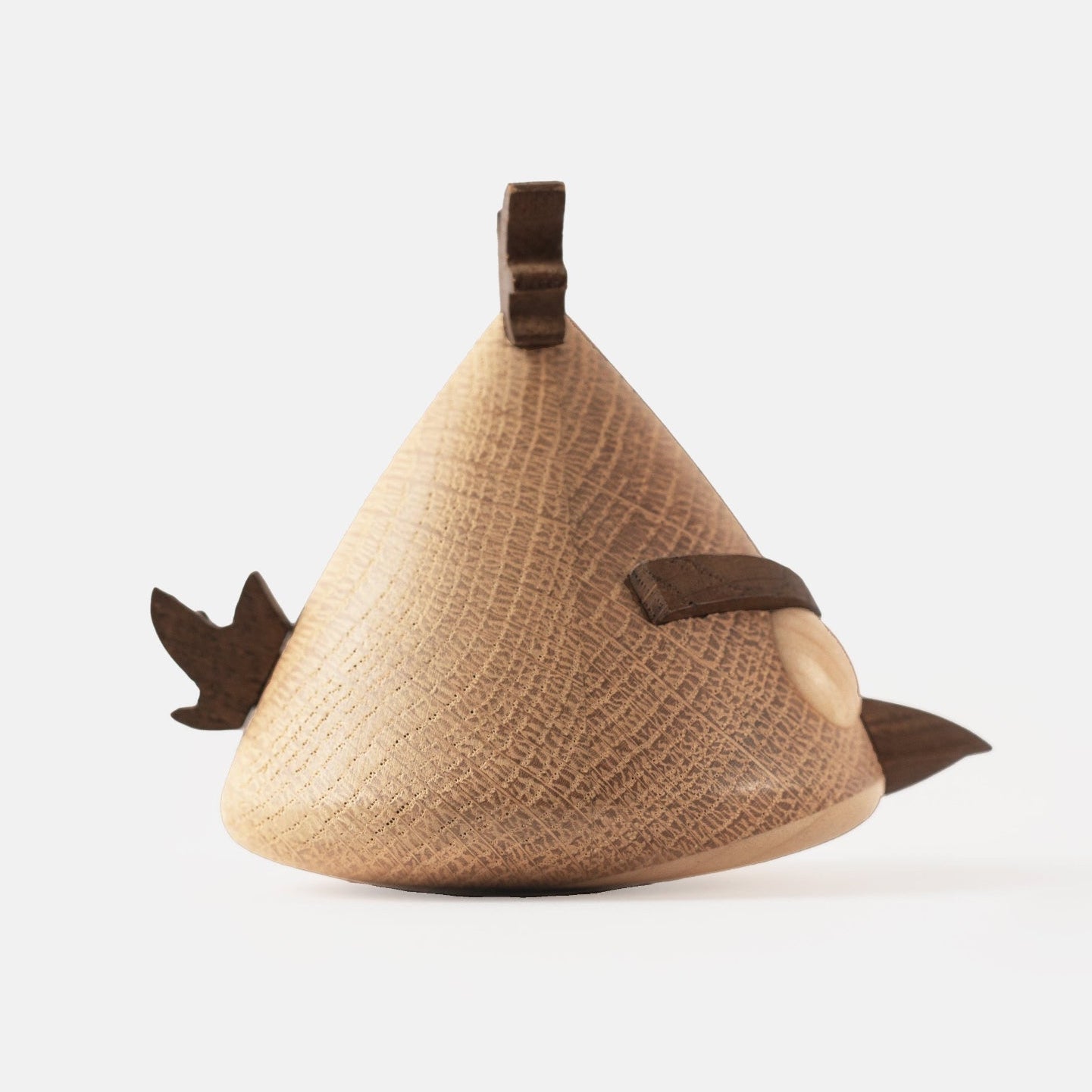 Side view of wooden figurine of an animated cartoon bird character carved from light and dark wood, featuring a triangular body shape, prominent angled eyebrows, round eye details, a small pointed beak, visible natural wood grain, and a smooth matte surface on a plain white background.