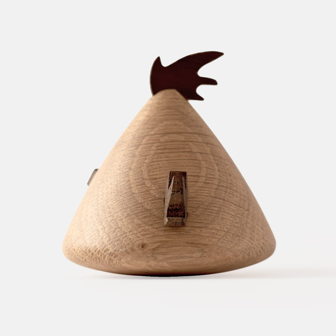 Back view of wooden figurine of an animated cartoon bird character carved from light and dark wood, featuring a triangular body shape, prominent angled eyebrows, round eye details, a small pointed beak, visible natural wood grain, and a smooth matte surface on a plain white background.