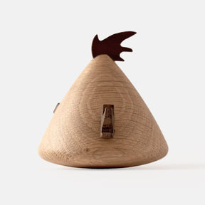Back view of wooden figurine of an animated cartoon bird character carved from light and dark wood, featuring a triangular body shape, prominent angled eyebrows, round eye details, a small pointed beak, visible natural wood grain, and a smooth matte surface on a plain white background.