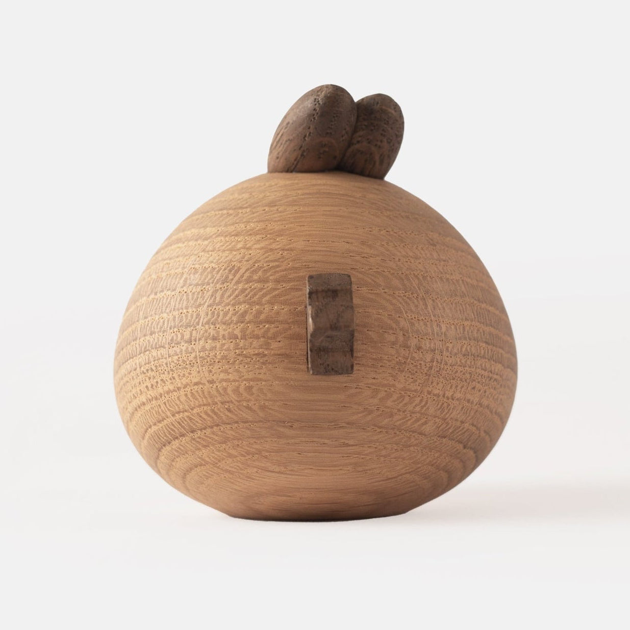 Back view of wooden figurine of an animated cartoon bird character carved from light and dark wood, featuring a round body, prominent angular eyebrows, circular eye details, a pointed beak, visible natural wood grain, and a smooth matte surface on a plain white background.