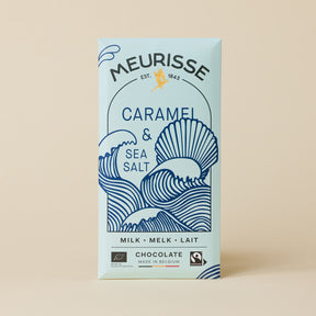 Meurisse caramel & sea salt milk chocolate bar in pale blue packaging, featuring navy illustrated ocean waves and a seashell, standing upright against a light beige background.