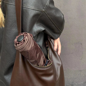 Brown leather bag with a rolled-up umbrella inside, worn by a person in a dark coat.