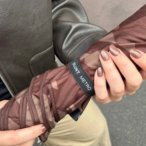 Person holding a brown umbrella with 'Quint Metro' branding, wearing a black leather jacket.