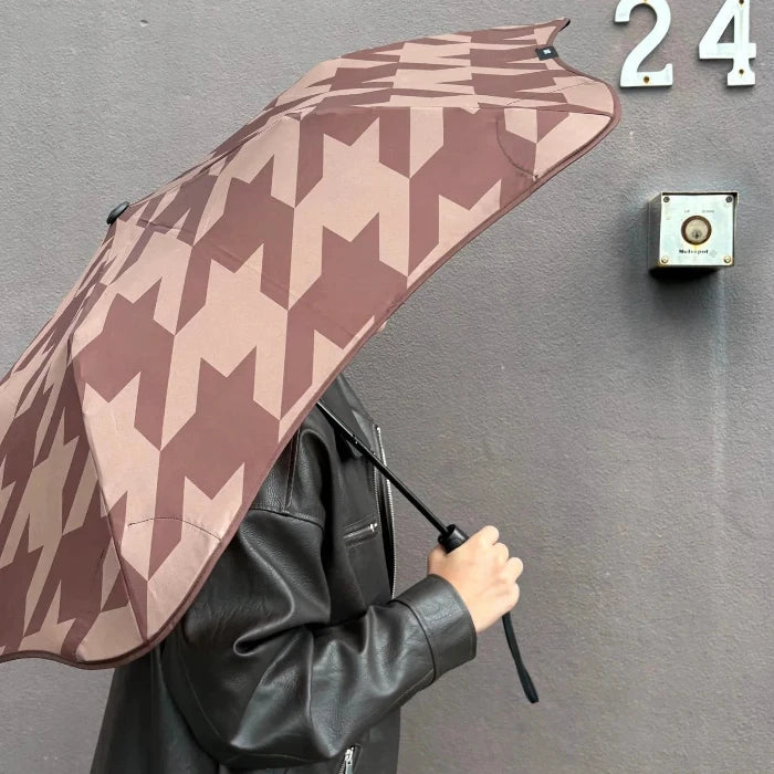 Person holding a patterned umbrella against a gray wall with a door number '24'.