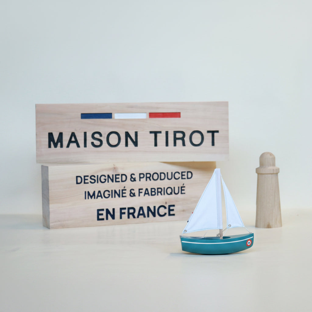 Model sailboat with a wooden sign displaying 'MAISON TIROT' and 'EN FRANCE' on a light background