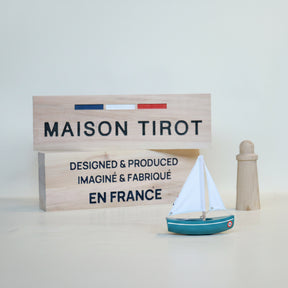 Model sailboat with a wooden sign displaying 'MAISON TIROT' and 'EN FRANCE' on a light background
