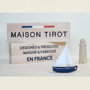 Model sailboat with a wooden sign displaying 'MAISON TIROT' and 'EN FRANCE' on a light background.