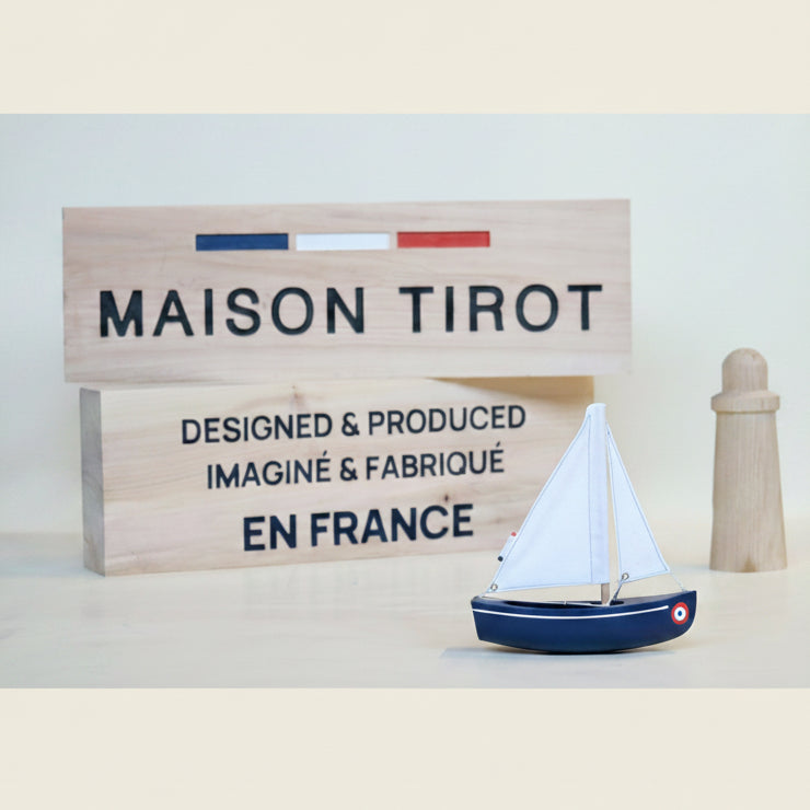 Model sailboat with a wooden sign displaying 'MAISON TIROT' and 'EN FRANCE' on a light background.
