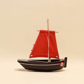 Model sailboat with a red sail on a beige background