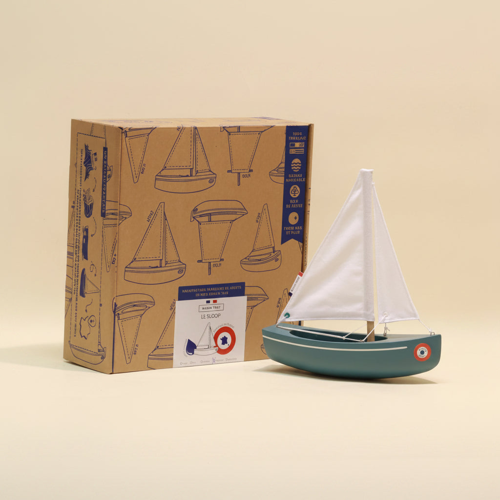 Model sailboat in front of its packaging box with sailboat illustrations on a beige background