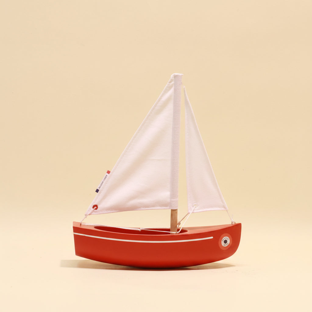 Red toy sailboat with white sails on a beige background