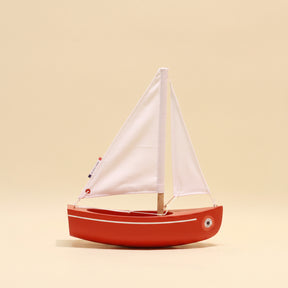 Red toy sailboat with white sails on a beige background