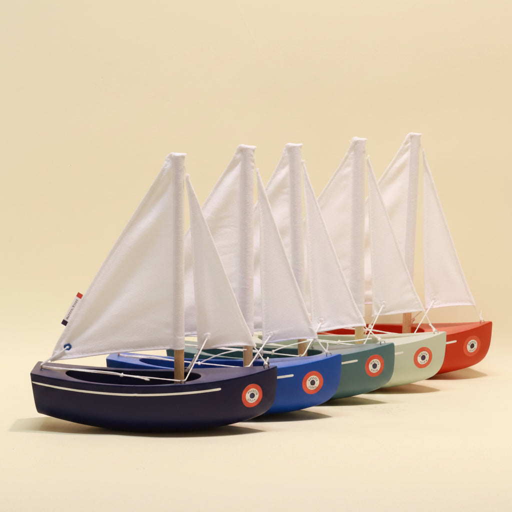 Four model sailboats with different colored hulls on a beige background