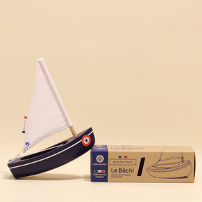 Model sailboat with a box labeled 'Le Béchi' on a beige background