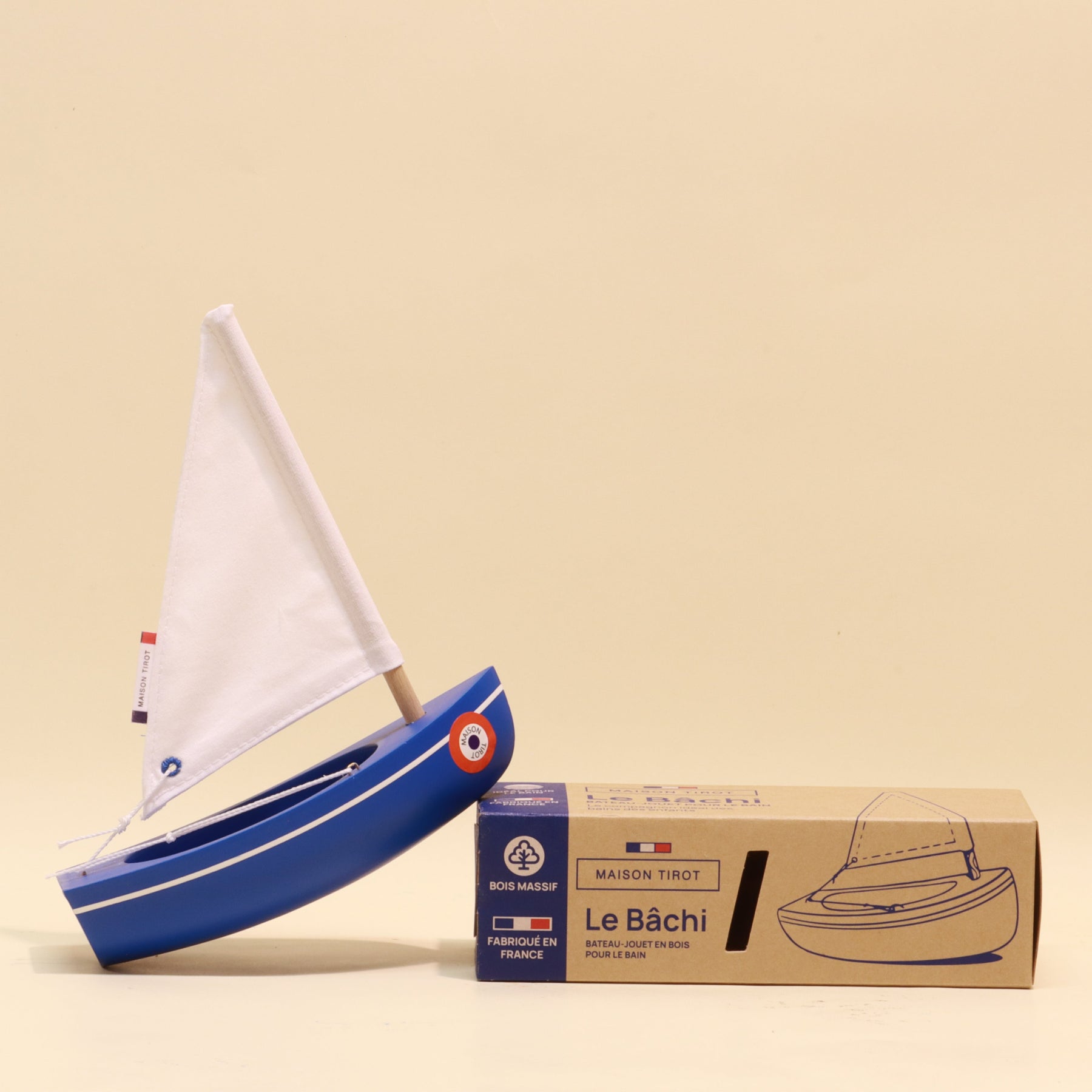 Model sailboat with white sail and blue body next to its packaging box on a beige background