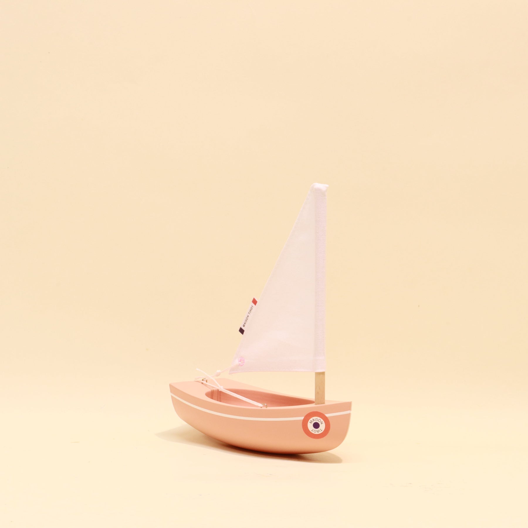 Small pink toy sailboat with a white sail on a beige background