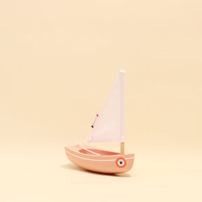 Small pink toy sailboat with a white sail on a beige background