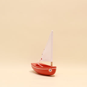 Small red toy sailboat with a white sail on a beige background