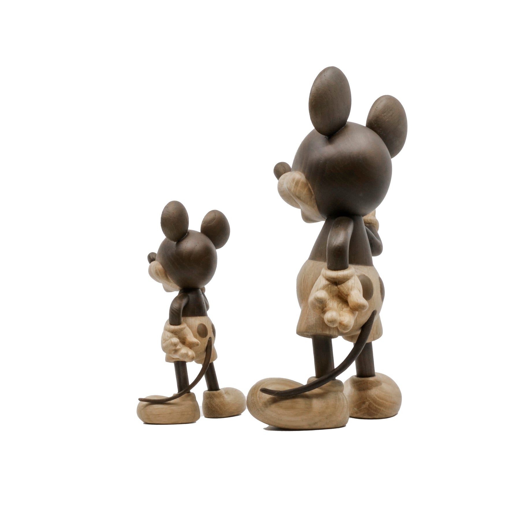 Two wooden figurines of an animated cartoon mouse character carved from contrasting light and dark wood, shown from the back, featuring rounded ears, gloved hands, short tails, oversized shoes, visible wood grain, and smooth matte surfaces on a plain white background.