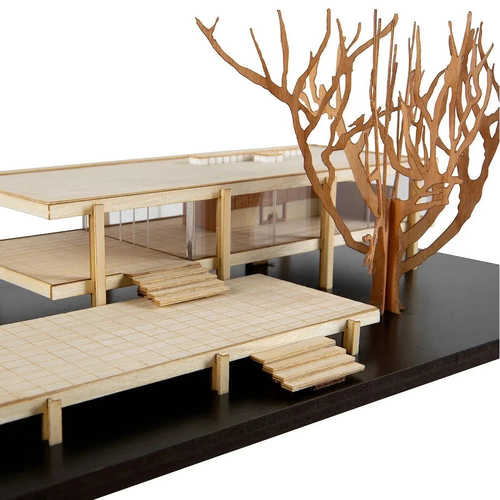 Model of a modern house with wooden furniture and decorative branches on a black base.