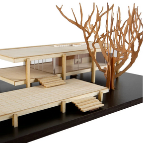 Model of a modern house with wooden furniture and decorative branches on a black base.