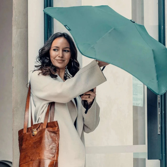 Woman holding a green umbrella and a brown leather bag in an urban setting.