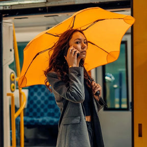 Woman holding a yellow umbrella inside a vehicle, talking on a phone.