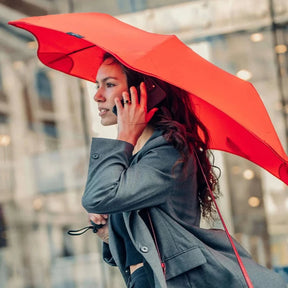 Woman holding a red umbrella and talking on a phone in an urban setting